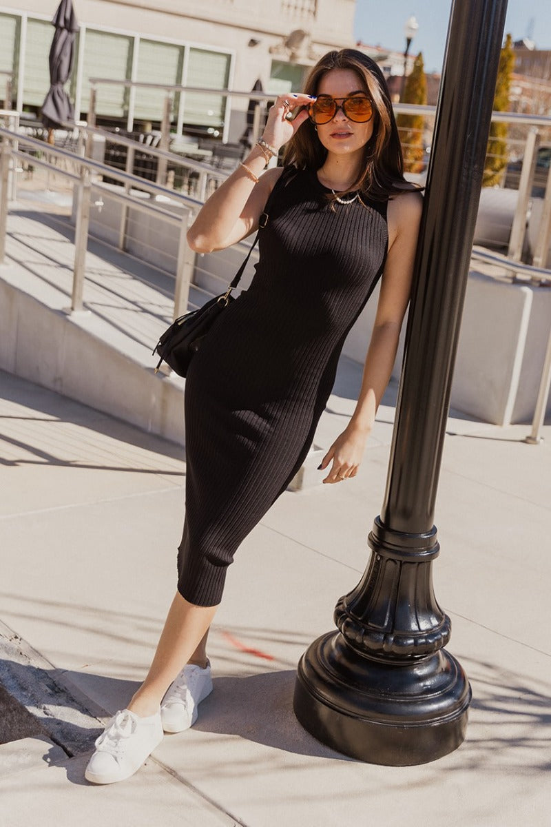 Full body front view of model wearing the Rachel Black Ribbed Sleeveless Midi Dress that features black ribbed knit fabric, midi length, a round neckline and a sleeveless body.