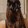 Image shows back of model's head wearing the Camila Black Satin Short Hair Bow that has short black satin fabric shaped as a bow and a clasp closure.