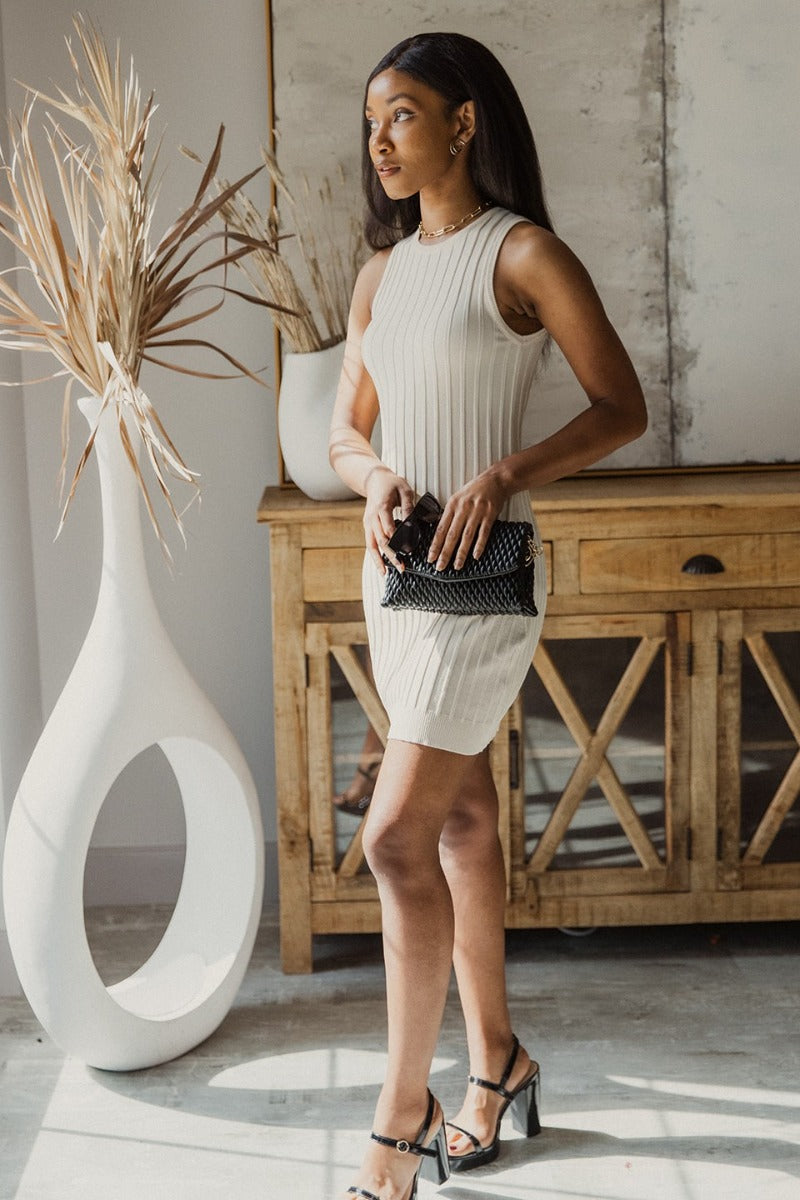Full body side view of model wearing the Keep It Classic Dress that has cream knit fabric with a thick ribbing design, mini length, a round neckline, and a sleeveless design.
