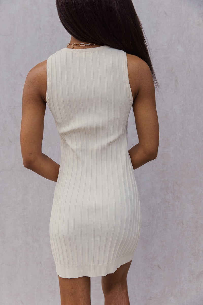 Back view of model wearing the Keep It Classic Dress that has cream knit fabric with a thick ribbing design, mini length, a round neckline, and a sleeveless design.