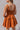 back view of model wearing the Falling For You Dress that has burnt orange fabric, mini length, burnt orange lining, a flare skirt with a tiered ruffle design, a square neckline, thick straps, and a monochromatic back zipper