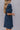 Side view of model wearing the Thinking Of You Dress that has indigo blue denim fabric with a textured design, mini length, an elastic waistband, pockets on each side, a square neckline and short puff sleeves with elastic hems.