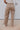 Back view of model wearing the Ready or Not Cargo Pants in Brown that have light brown denim fabric, cargo pockets on each side, a front zipper with a button closure, two front pockets, belt loops and wide pant legs