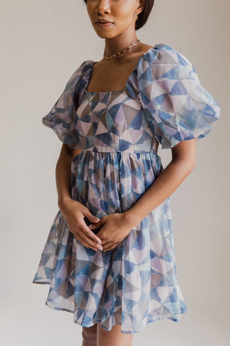 front view of model wearing the I'm In Wonderland Dress that has sheer geometric pattern, mauve pink lining, mini length, a square neckline, short puff sleeves, and a smocked back