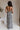 Full back view of model wearing the All I Want Maxi Dress that has a cream and black floral print, maxi length, a slit on the side, an elastic waist, a halter neckline with cutout details, adjustable straps, and an open back