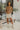Full body front view of model wearing the Hard To Get Pleather Skirt that has taupe pleather fabric, mini length, two front pockets, two back pockets, a front zipper with a button closure and belt loops