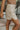 Side view of model wearing the Hard To Get Pleather Skirt that has taupe pleather fabric, mini length, two front pockets, two back pockets, a front zipper with a button closure and belt loops