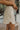 Side view of model wearing the Hard To Get Pleather Skirt that has taupe pleather fabric, mini length, two front pockets, two back pockets, a front zipper with a button closure and belt loops