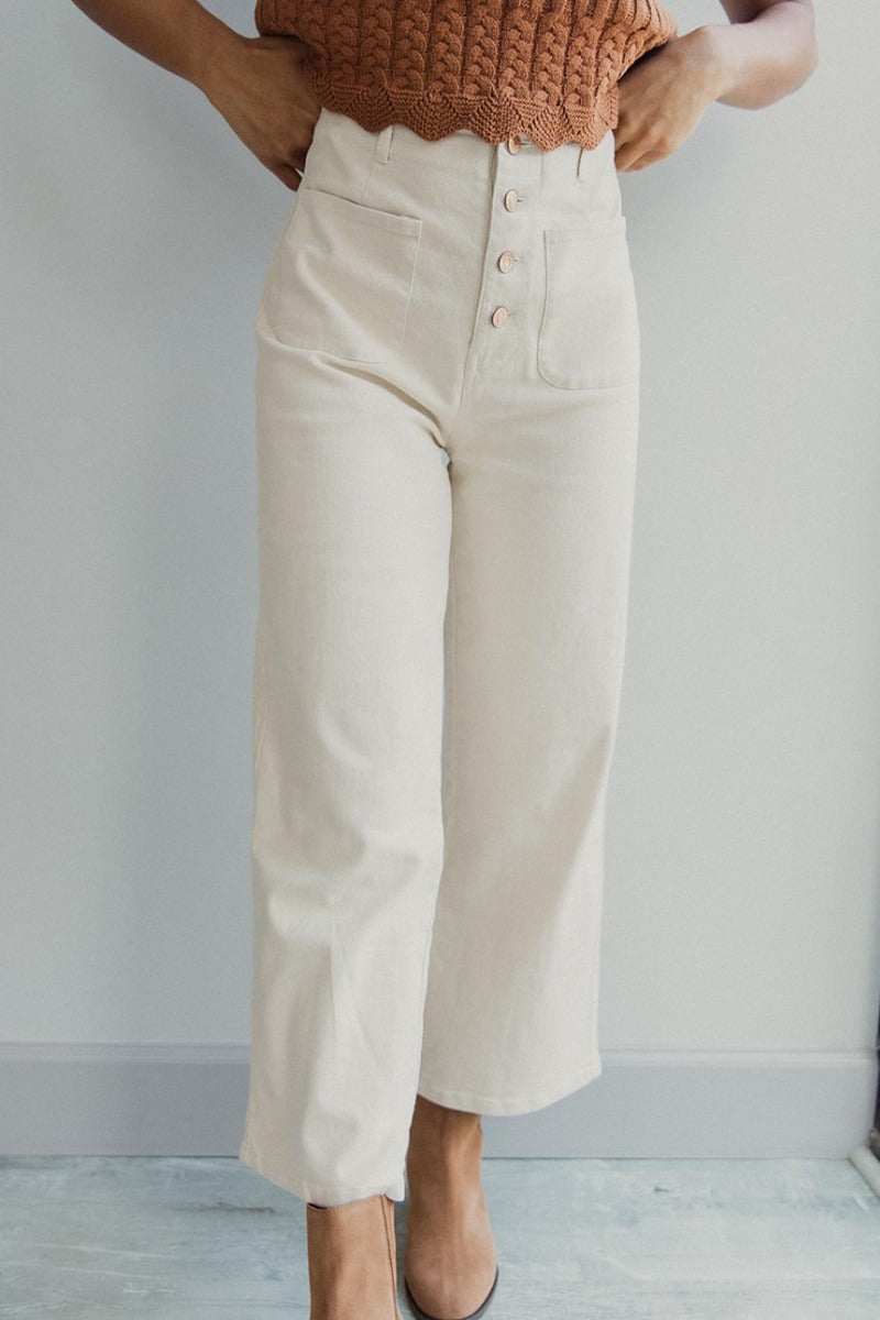 Front view of model wearing the Good Day Pants in Cream that have cream denim fabric, pockets, copper button up closures, belt loops and wide cropped flares.