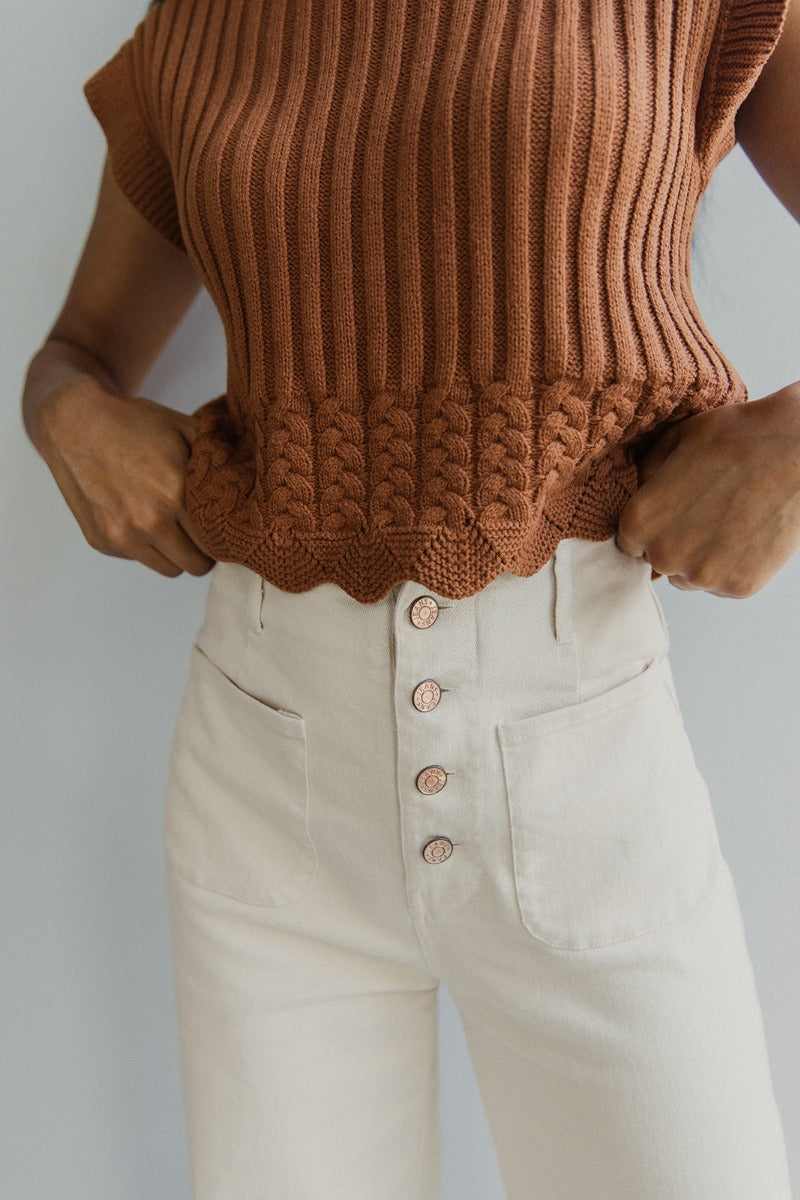 Upper front view of model wearing the Good Day Pants in Cream that have cream denim fabric, pockets, copper button up closures, belt loops and wide cropped flares.