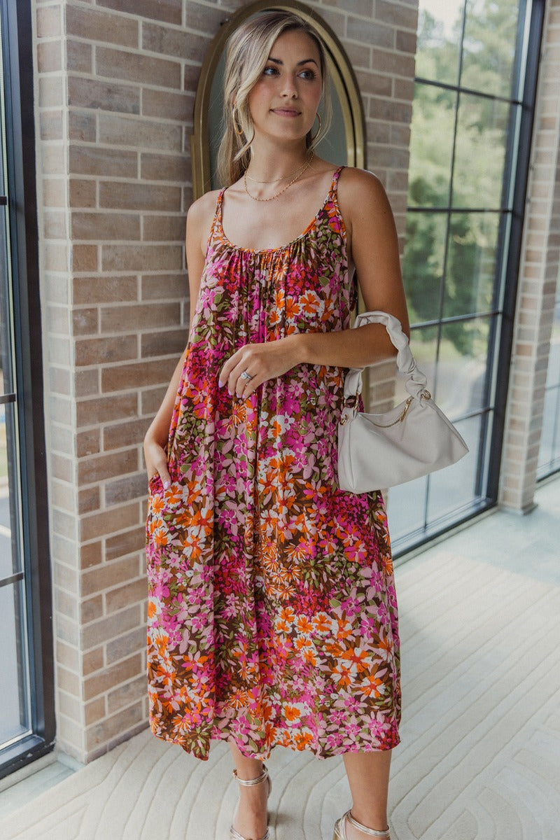 Full body view of model wearing the Everything To Me Floral Dress which features a brown, orange, pink, green and white floral print, midi length, a scooped neckline, and adjustable straps.