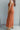 Side view of model wearing the Unexpected Treasure Jumpsuit which features rust ribbed fabric, wide cropped pants, pockets on each side, a v-neckline, and spaghetti straps.