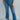 Front view of model wearing the Ceros: Break Even Jeans which features medium blue washed denim, a front zipper with a button closure, belt loops, a high-rise waist, two front pockets, two back pockets, brown stitching and cropped flares.