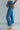 Side view of model wearing the Ceros: Break Even Jeans which features medium blue washed denim, a front zipper with a button closure, belt loops, a high-rise waist, two front pockets, two back pockets, brown stitching and cropped flares.