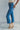 Side view of model wearing the Ceros: Break Even Jeans which features medium blue washed denim, a front zipper with a button closure, belt loops, a high-rise waist, two front pockets, two back pockets, brown stitching and cropped flares.