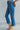 Side view of model wearing the Ceros: Break Even Jeans which features medium blue washed denim, a front zipper with a button closure, belt loops, a high-rise waist, two front pockets, two back pockets, brown stitching and cropped flares.