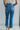 Back view of model wearing the Ceros: Break Even Jeans which features medium blue washed denim, a front zipper with a button closure, belt loops, a high-rise waist, two front pockets, two back pockets, brown stitching and cropped flares.