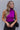 Front view of model wearing the Tell Me More Bodysuit in Violet which features magenta knit fabric, a turtleneck, a sleeveless design, and a thong bottom with snap closures.