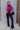 Full body view of model wearing the Tell Me More Bodysuit in Violet which features magenta knit fabric, a turtleneck, a sleeveless design, and a thong bottom with snap closures.
