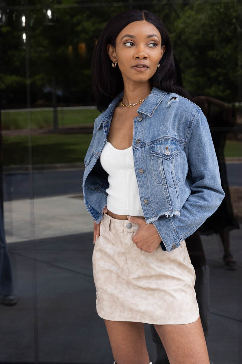 Front view of model wearing the Wish You Were Here Denim Jacket which features washed denim fabric, a cropped waist, distressed details, button up closures, two front buttoned pockets, a collared neckline and long sleeve with buttoned cuffs.
