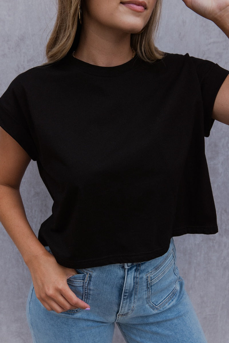 Front view of model wearing the See You Later Tee that has black cotton fabric, a cropped waist, a round neckline and short folded sleeves