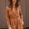 Front view of model wearing the More Than Enough Romper In Camel, which has a camel corduroy material, a collar neck, a surplice front, a long sleeve with a button, a front zipper, pockets, and pleating on the legs.