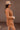 Side view of model wearing the More Than Enough Romper In Camel, which has a camel corduroy material, a collar neck, a surplice front, a long sleeve with a button, a front zipper, pockets, and pleating on the legs.