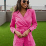  Frontal view of the More Than Enough Romper that features a pink corduroy material, a collar neck, a surplice front, a long sleeve with a button, a front zipper, pockets, and pleating on the legs.