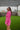 Side view of the More Than Enough Romper that features a pink corduroy material, a collar neck, a surplice front, a long sleeve with a button, a front zipper, pockets, and pleating on the legs.