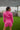  Back view of the More Than Enough Romper that features a pink corduroy material, a collar neck, a surplice front, a long sleeve with a button, a front zipper, pockets, and pleating on the legs.
