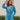 Frontal view of the More Than Enough Romper that features a blue corduroy material, a collar neck, a surplice front , a long sleeve with a button, a front zipper, pockets, and pleating on the legs.