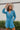 Frontal view of the More Than Enough Romper that features a blue corduroy material, a collar neck, a surplice front , a long sleeve with a button, a front zipper, pockets, and pleating on the legs.