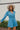 Frontal view of the More Than Enough Romper that features a blue corduroy material, a collar neck, a surplice front , a long sleeve with a button, a front zipper, pockets, and pleating on the legs.