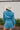 Back view of the More Than Enough Romper that features a blue corduroy material, a collar neck, a surplice front , a long sleeve with a button, a front zipper, pockets, and pleating on the legs.