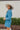 Side view of the More Than Enough Romper that features a blue corduroy material, a collar neck, a surplice front , a long sleeve with a button, a front zipper, pockets, and pleating on the legs.