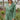 Frontal view of the More Than Enough Romper that features a green corduroy material, a collar neck, a surplice front, a long sleeve with a button, a front zipper, pockets, and pleating on the legs.