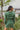 Back view of the More Than Enough Romper that features a green corduroy material, a collar neck, a surplice front, a long sleeve with a button, a front zipper, pockets, and pleating on the legs.