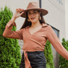 Front view of model wearing the Walk Away Top, which features a copper colored material, a collar neck, a surplice neckline, long sleeves, and a front tie closure.