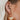 The Seasons Change Earring is a gold dangle style earring, featuring an open gold arch, a gold half circle body, and a brown beading at the edge.