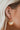 The Seasons Change Earring is a gold dangle style earring, featuring an open gold arch, a gold half circle body, and a brown beading at the edge.