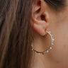 Close side view of model wearing the Color Your World Hoop Earrings, which feature thin open gold hoops with multi-colored dots.