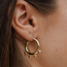 Close side view of model wearing the Belle Of The Ball Earrings, which feature gold hoops with four gold beads along the bottom.