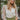 Front view of model wearing the Someday Soon Bodysuit that has cream satin fabric with a surplice neckline, a knit thong bottom with snap closures, and organza puff sleeves. Worn under green skirt.