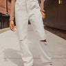 Front view of model wearing the Most Wanted Jeans, that have white denim, a crossover waist, a high-rise fit, a button closure, two front pockets, distressing at the knees, two back pockets, and a straight leg fit.