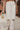 Clseo-up front view of model wearing the Most Wanted Jeans, that have white denim, a crossover waist, a high-rise fit, a button closure, two front pockets, distressing at the knees, two back pockets, and a straight leg fit.
