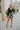 Full body front view of model wearing the Feeling It Floral Skirt, which features black satin fabric with a multi-colored floral print, a black lining, a small side slit, and a side zipper