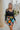Front view of model wearing the Feeling It Floral Skirt, which features black satin fabric with a multi-colored floral print, a black lining, a small side slit, and a side zipper