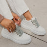 Side view of the Newport Sneakers, which have white uppers, white chunky soles, sage green laces, and a sage green heel tab. Shoe are shown on model's feet.