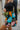 Close side view of model wearing the Feeling It Floral Skirt, which features black satin fabric with a multi-colored floral print, a black lining, a small side slit, and a side zipper