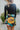 Back view of model wearing the Feeling It Floral Skirt, which features black satin fabric with a multi-colored floral print, a black lining, a small side slit, and a side zipper